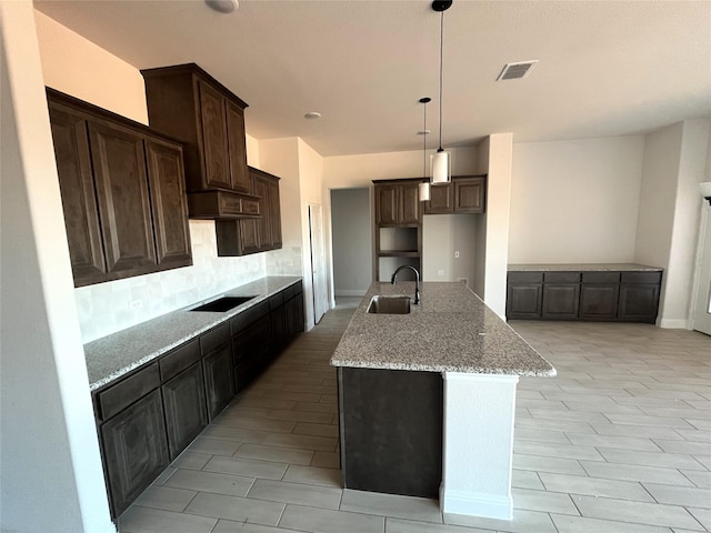 kitchen featuring sink, light stone counters, hanging light fixtures, a center island with sink, and black electric stovetop