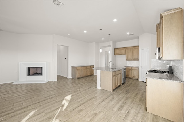 kitchen with sink, a kitchen island with sink, backsplash, stainless steel appliances, and decorative light fixtures