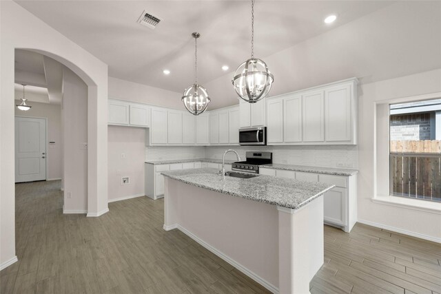 kitchen with decorative light fixtures, appliances with stainless steel finishes, a kitchen island with sink, and white cabinetry