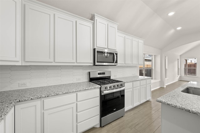 kitchen with vaulted ceiling, tasteful backsplash, white cabinets, light stone counters, and stainless steel appliances