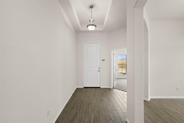 corridor with dark wood-type flooring and a tray ceiling