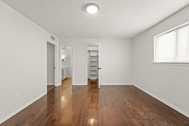 unfurnished bedroom with a walk in closet, a closet, and dark wood-type flooring