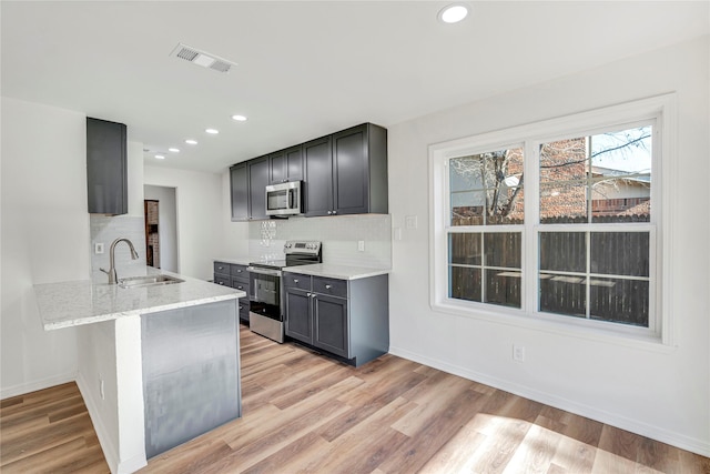 kitchen with light stone countertops, sink, tasteful backsplash, light hardwood / wood-style floors, and appliances with stainless steel finishes