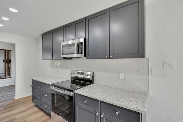 kitchen with gray cabinetry, decorative backsplash, light hardwood / wood-style floors, light stone counters, and stainless steel appliances