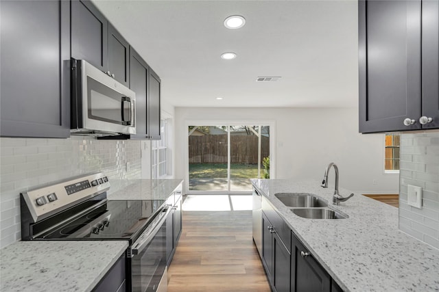 kitchen with sink, appliances with stainless steel finishes, tasteful backsplash, light hardwood / wood-style floors, and light stone counters