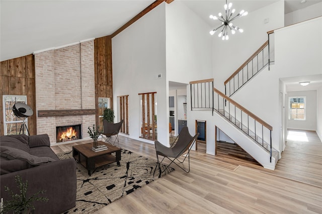 living room with high vaulted ceiling, light wood-type flooring, a notable chandelier, and a brick fireplace