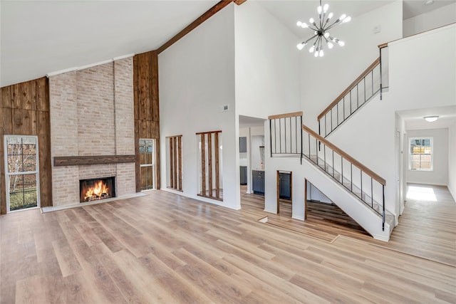 unfurnished living room featuring a fireplace, high vaulted ceiling, light wood-type flooring, and a notable chandelier