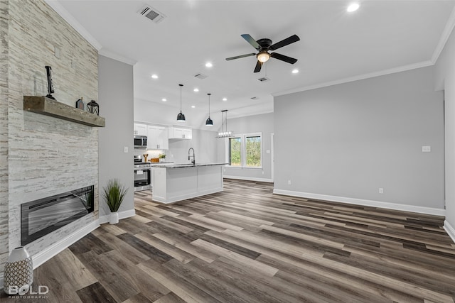 unfurnished living room with sink, a stone fireplace, dark hardwood / wood-style flooring, ceiling fan with notable chandelier, and ornamental molding