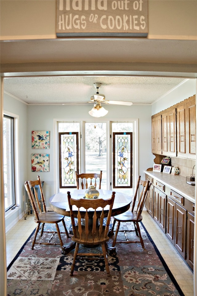 tiled dining space featuring ceiling fan, crown molding, and a textured ceiling