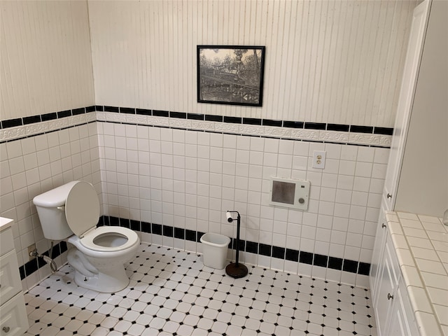 bathroom featuring tile patterned floors, toilet, and tile walls