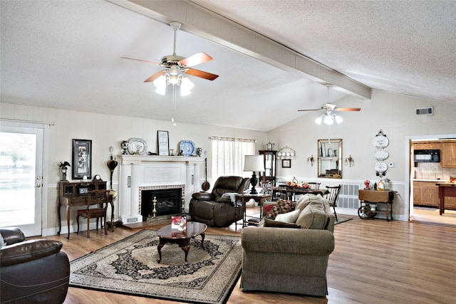 living room featuring a fireplace, a textured ceiling, vaulted ceiling with beams, and light hardwood / wood-style floors