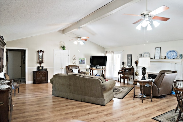 living room with light wood-type flooring, a brick fireplace, a textured ceiling, ceiling fan, and vaulted ceiling with beams