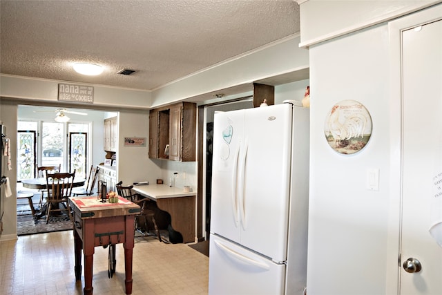 kitchen with a textured ceiling, white fridge with ice dispenser, crown molding, and ceiling fan