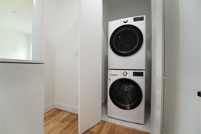 washroom with hardwood / wood-style floors and stacked washing maching and dryer