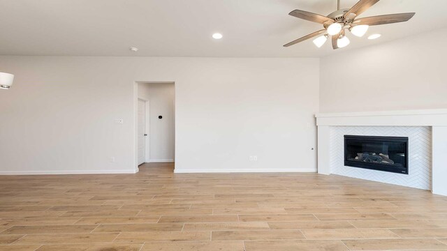unfurnished living room featuring a tiled fireplace, light wood-style flooring, baseboards, ceiling fan, and recessed lighting