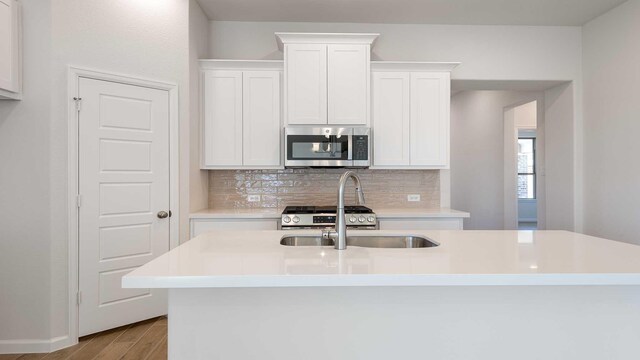 kitchen with light countertops, decorative backsplash, a sink, appliances with stainless steel finishes, and wood finished floors