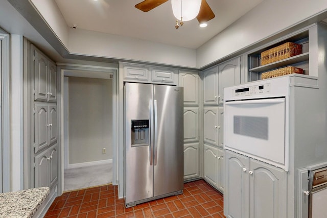 kitchen with stainless steel refrigerator with ice dispenser, oven, ceiling fan, and gray cabinetry