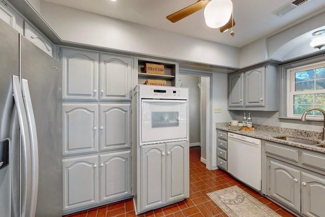 kitchen with light stone countertops, gray cabinetry, white appliances, ceiling fan, and sink