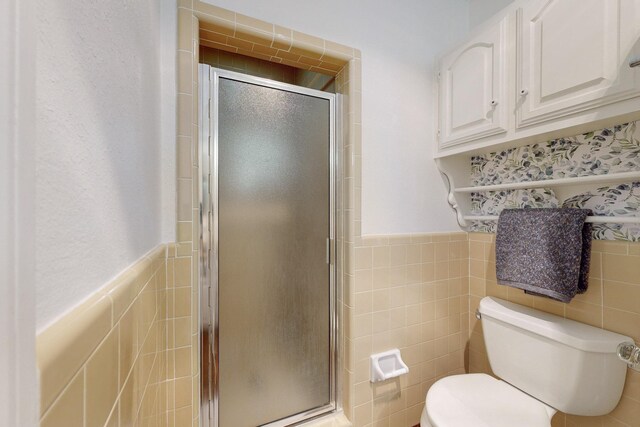 bathroom featuring walk in shower, toilet, and tile walls