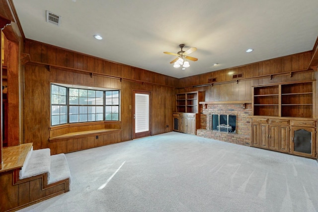 unfurnished living room with ceiling fan, light colored carpet, wooden walls, and a brick fireplace