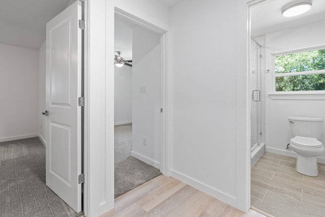 bathroom featuring hardwood / wood-style flooring, toilet, a shower with door, and ceiling fan