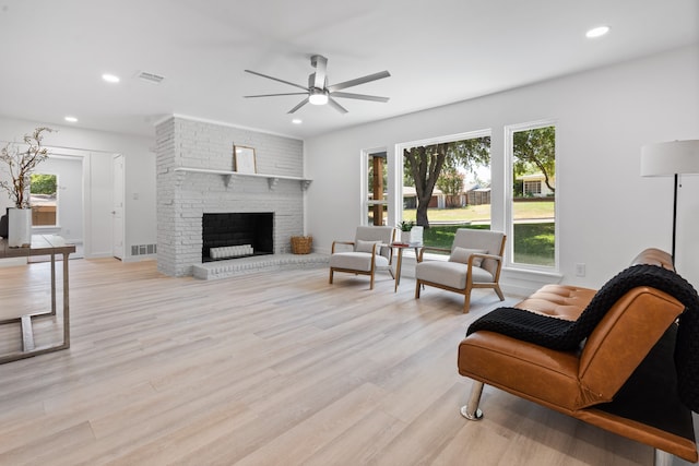 living room featuring ceiling fan, light hardwood / wood-style floors, and a brick fireplace