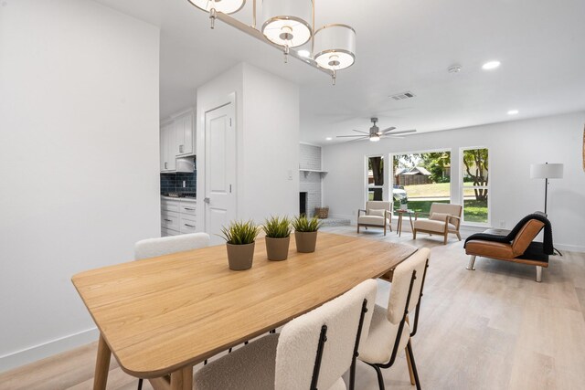 dining space with light wood-type flooring, a brick fireplace, and ceiling fan