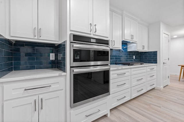 kitchen with white cabinets, light hardwood / wood-style flooring, tasteful backsplash, light stone counters, and stainless steel appliances