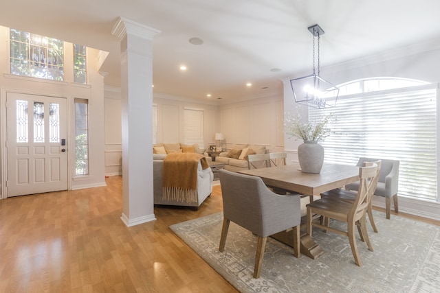 dining area featuring light wood-type flooring, decorative columns, a wealth of natural light, and crown molding