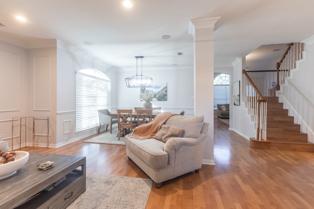 living room with hardwood / wood-style floors, an inviting chandelier, ornamental molding, and ornate columns