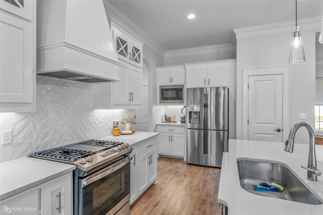 kitchen with custom range hood, stainless steel appliances, sink, light hardwood / wood-style flooring, and white cabinetry