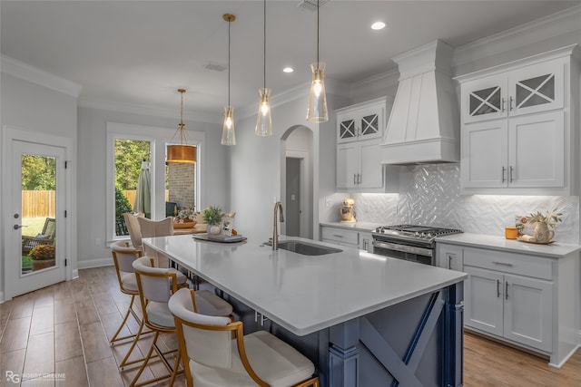 kitchen with a kitchen island with sink, white cabinets, sink, decorative light fixtures, and custom range hood