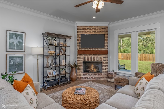 living room featuring hardwood / wood-style floors, ceiling fan, crown molding, and a brick fireplace