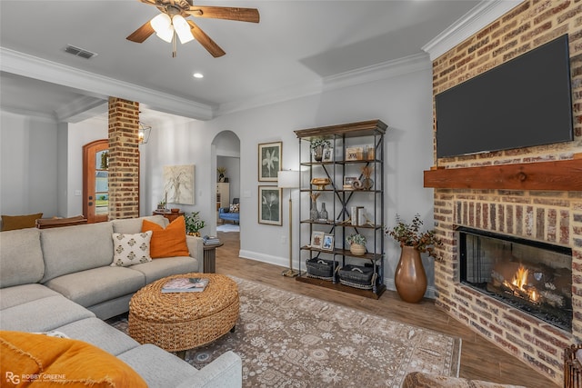 living room with a brick fireplace, ceiling fan, hardwood / wood-style floors, and ornamental molding