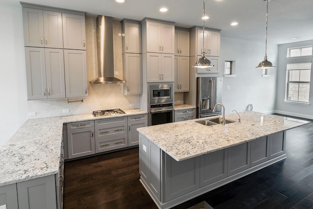 kitchen featuring appliances with stainless steel finishes, dark hardwood / wood-style flooring, wall chimney exhaust hood, and an island with sink