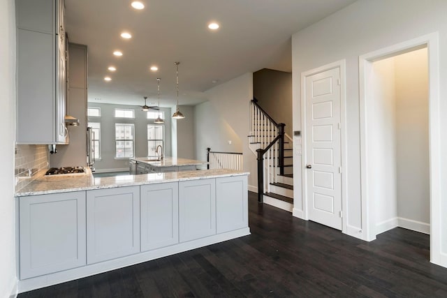 kitchen with kitchen peninsula, light stone counters, stainless steel gas cooktop, decorative light fixtures, and dark hardwood / wood-style floors