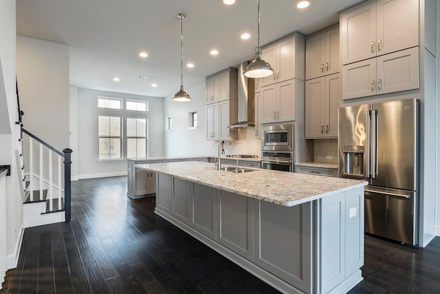 kitchen featuring gray cabinetry, wall chimney range hood, light stone counters, pendant lighting, and appliances with stainless steel finishes