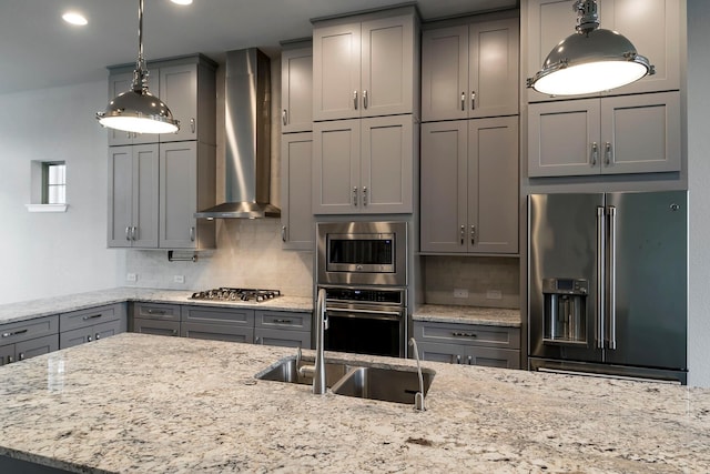 kitchen with pendant lighting, wall chimney exhaust hood, decorative backsplash, light stone countertops, and appliances with stainless steel finishes