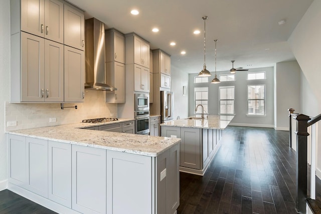 kitchen with wall chimney exhaust hood, gray cabinets, decorative light fixtures, and appliances with stainless steel finishes