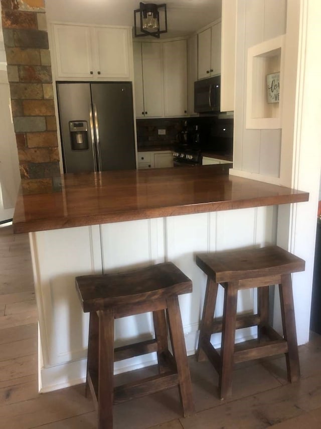 kitchen featuring black appliances, a kitchen bar, kitchen peninsula, and hardwood / wood-style flooring