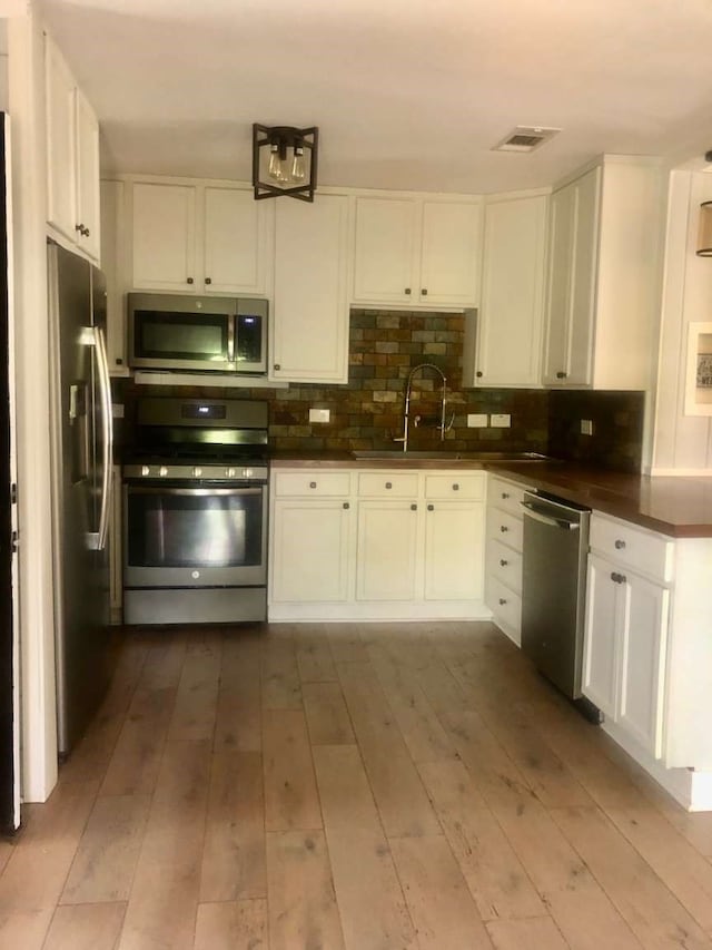 kitchen featuring sink, appliances with stainless steel finishes, tasteful backsplash, light hardwood / wood-style floors, and white cabinetry