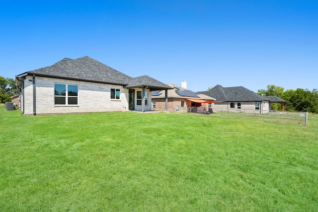 rear view of property with central air condition unit, a yard, and solar panels