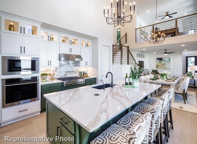 kitchen with appliances with stainless steel finishes, light wood-type flooring, decorative light fixtures, and a kitchen island with sink