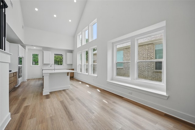 4182 Carter Ct, Denison, TX 75020 - kitchen featuring high vaulted ceiling, white cabinetry, light wood-type flooring, a sink, and a kitchen island with sink