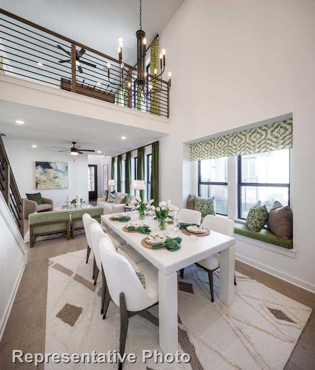 dining space featuring ceiling fan with notable chandelier, hardwood / wood-style floors, and a towering ceiling