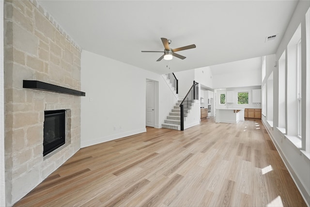 4182 Carter Ct, Denison, TX 75020 - unfurnished living room with a stone fireplace, stairs, light wood-style floors, a ceiling fan, and baseboards
