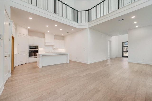 unfurnished living room with light hardwood / wood-style floors and a high ceiling