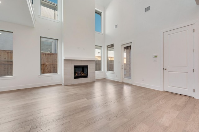 unfurnished living room featuring a wealth of natural light, light hardwood / wood-style flooring, a tile fireplace, and a high ceiling