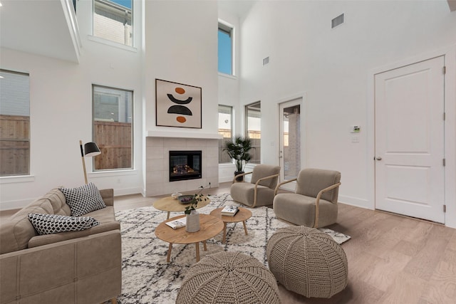 living room with a towering ceiling, light hardwood / wood-style floors, and a tile fireplace