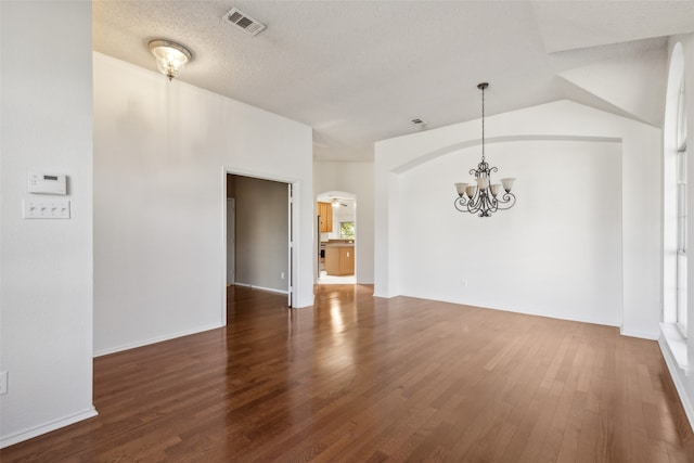 spare room with lofted ceiling, dark hardwood / wood-style flooring, a chandelier, and a textured ceiling